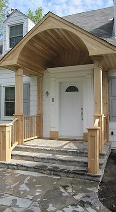 a white house with a wooden porch and covered front entryway that has stone steps leading up to the front door