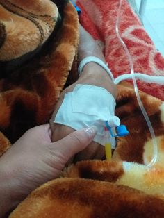 a person with an iv in their hand on top of a bed next to a stuffed animal