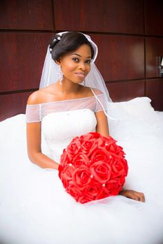 a woman sitting on top of a bed holding a red bouquet