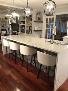 a kitchen island with four stools in the center and an open floor plan behind it