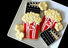 some cookies that are shaped like popcorns and movie tickets on a white square plate