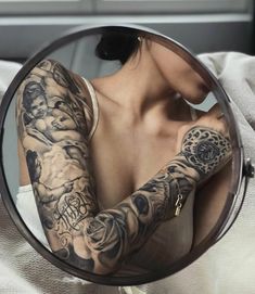 a woman with tattoos on her arm looking in a mirror and holding onto the camera