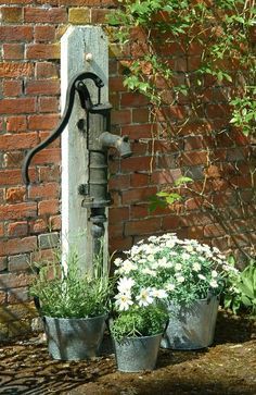 an old water faucet with flowers in buckets next to it on the side of a brick wall