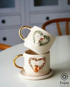 two white cups with gold handles sitting on top of a table next to each other