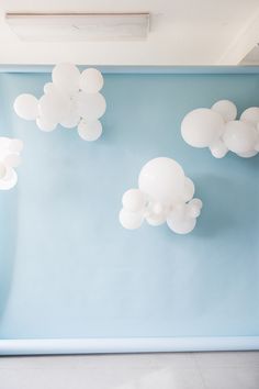 white balloons are floating in the air above a blue wall with clouds painted on it