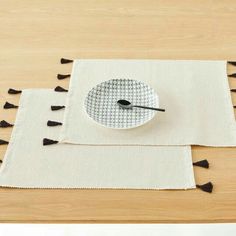 a place mat with black tassels and a white plate on it sitting on top of a wooden table