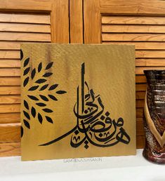 an arabic calligraphy is displayed next to a vase and painting on a wooden panel