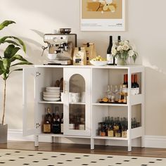 a white shelf with bottles and glasses on it in a room next to a potted plant