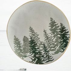 a plate with trees painted on it hanging from the ceiling in front of snow covered ground