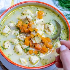 a hand holding a spoon over a bowl of chicken and dumpling soup with carrots