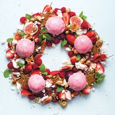 a wreath made out of strawberries and other fruits on a white surface with green leaves