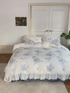 a white bed with blue flowers on it in a room next to a door and potted plant