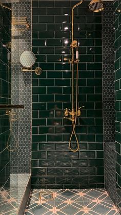 a bathroom with green tile and gold fixtures on the shower head, hand held by a brass faucet