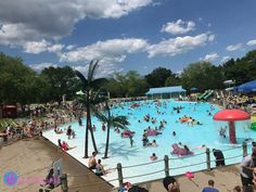 an outdoor swimming pool with many people in it and some trees around the pool area