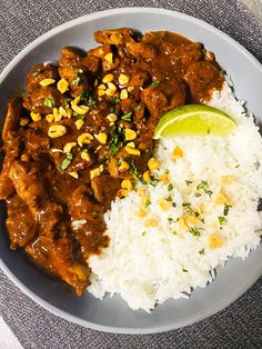 a white plate topped with rice and meat next to a slice of lime on top of it