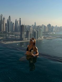 a woman sitting on the edge of a swimming pool in front of a city skyline