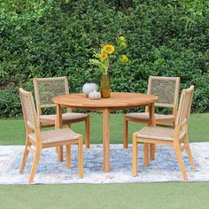 a wooden table with four chairs around it on a rug in front of some bushes