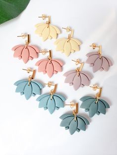 six pairs of earrings with leaves attached to each earring, on a white surface