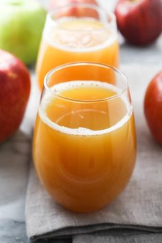 three glasses filled with orange juice sitting on top of a napkin next to apples and an apple