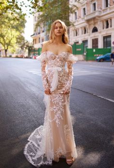 a woman standing on the street wearing a dress with sheer sleeves and an off shoulder