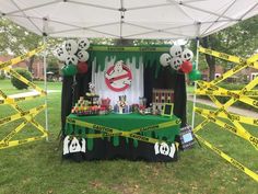 a green and black booth with yellow caution tape on the grass, soccer balls hanging from it's ceiling