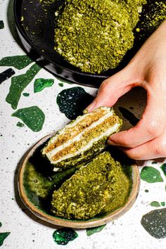 a person is picking up some food from a plate with green stuff on it and other foods in the background