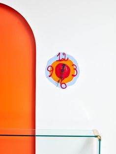 an orange and red clock sitting on the side of a wall next to a glass shelf