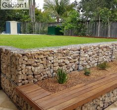 a stone wall and wooden bench in the middle of a yard with grass growing on it