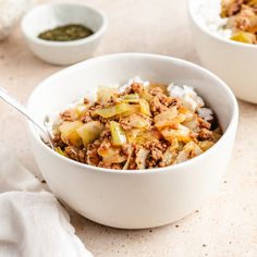 two white bowls filled with food on top of a table next to some napkins