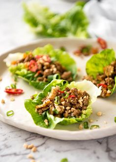 three lettuce wraps filled with meat and vegetables on a white plate next to some red peppers