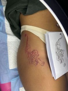 a woman's stomach with a tiger tattoo on it and a book laying next to her