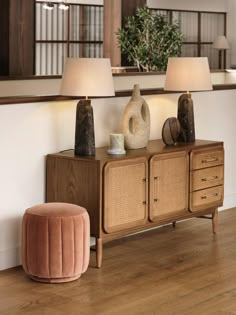 a living room with two lamps on top of the table and a sideboard in front of it