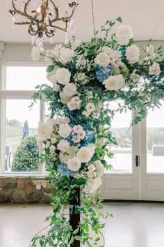 an arrangement of white and blue flowers on a pole in front of a chandelier