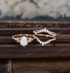 two wedding rings on top of a wooden table with flowers in the backgroud