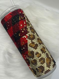 a red and brown leopard print tumbler cup sitting on top of a white fur covered floor