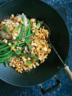 a black plate topped with green beans and other food on top of a blue table