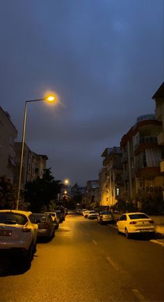 cars are parked on the street in front of buildings at night, with one car driving down the road