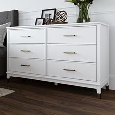 a bedroom scene with focus on the dresser and bed sideboard that has flowers in it