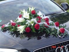 a bouquet of roses and lilies on the hood of a car with ribbons tied around it