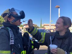 two women in firefighter gear are eating something out of a paper cup with a spoon