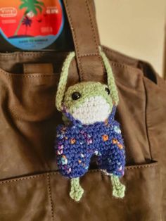 a small crocheted frog is hanging from a brown leather tote bag with a cd in the background