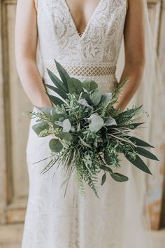 a woman in a wedding dress holding a bridal bouquet with greenery and white flowers