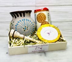 a ceramic vase and some other items in a box on a white table with wood shavings