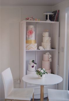 a white table topped with lots of cake next to a shelf filled with different types of cakes