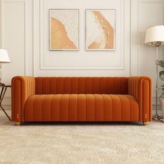 an orange couch in a white room with two pictures on the wall and a lamp next to it