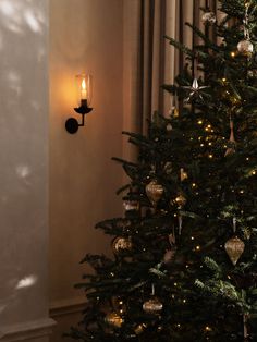 a lit christmas tree in the corner of a room with a wall light on it