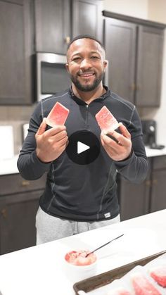 a man standing in front of a kitchen counter holding up two pieces of red food