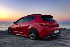 the rear end of a red car parked on top of a beach near the ocean