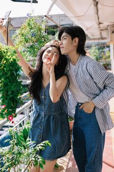 a man and woman standing next to each other in front of plants on the ground