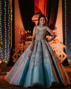 a woman standing in front of a stage wearing a blue and gold gown with long sleeves